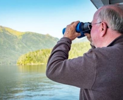 Man looking through binoculars on a houseboat birdwatching